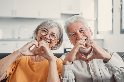Bild eines Rentnerpaares, das mit den Händen das Herzzeichen formt und in die Kamera lacht.